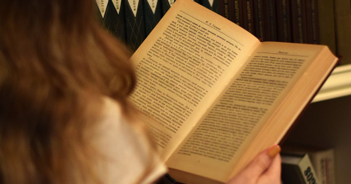 Young woman reading in front of a bookshelf filled with books