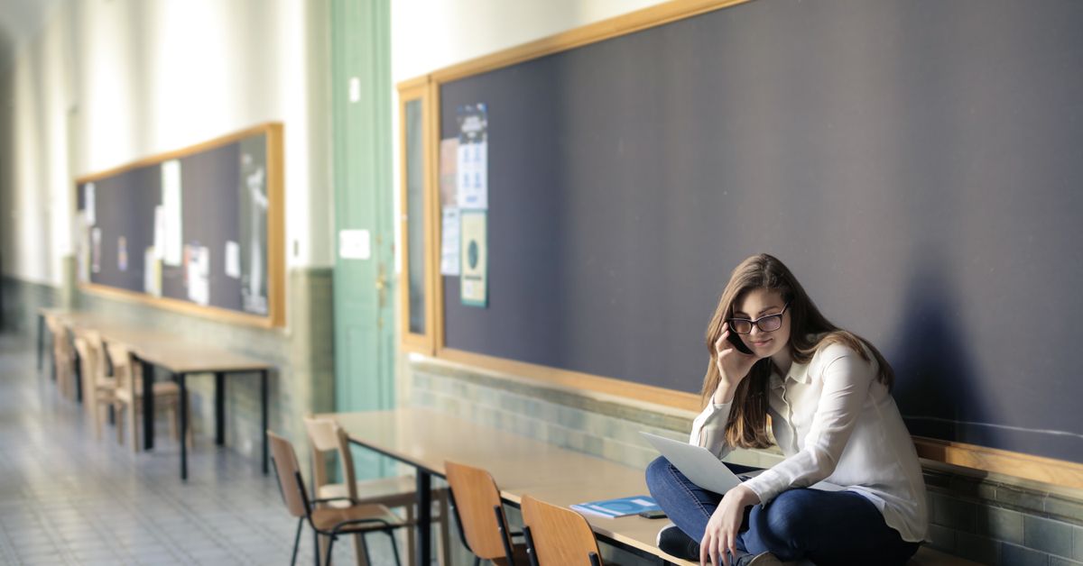 Woman studying at a desk in a university hallway with a laptop and notes