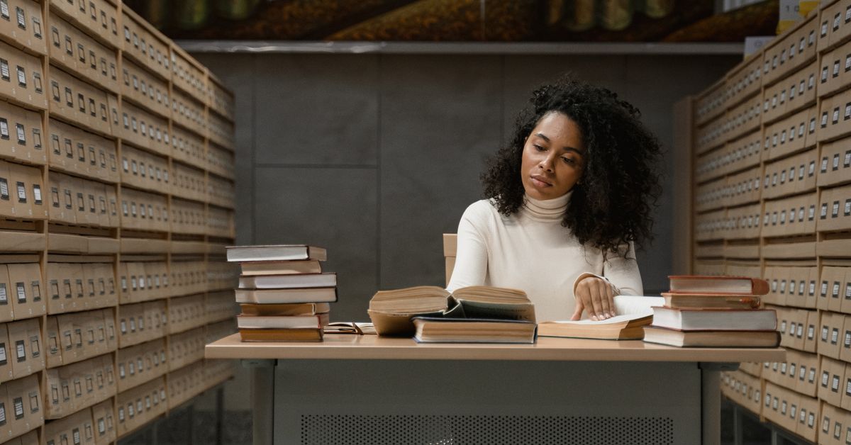 Woman reading at a desk surrounded by library books