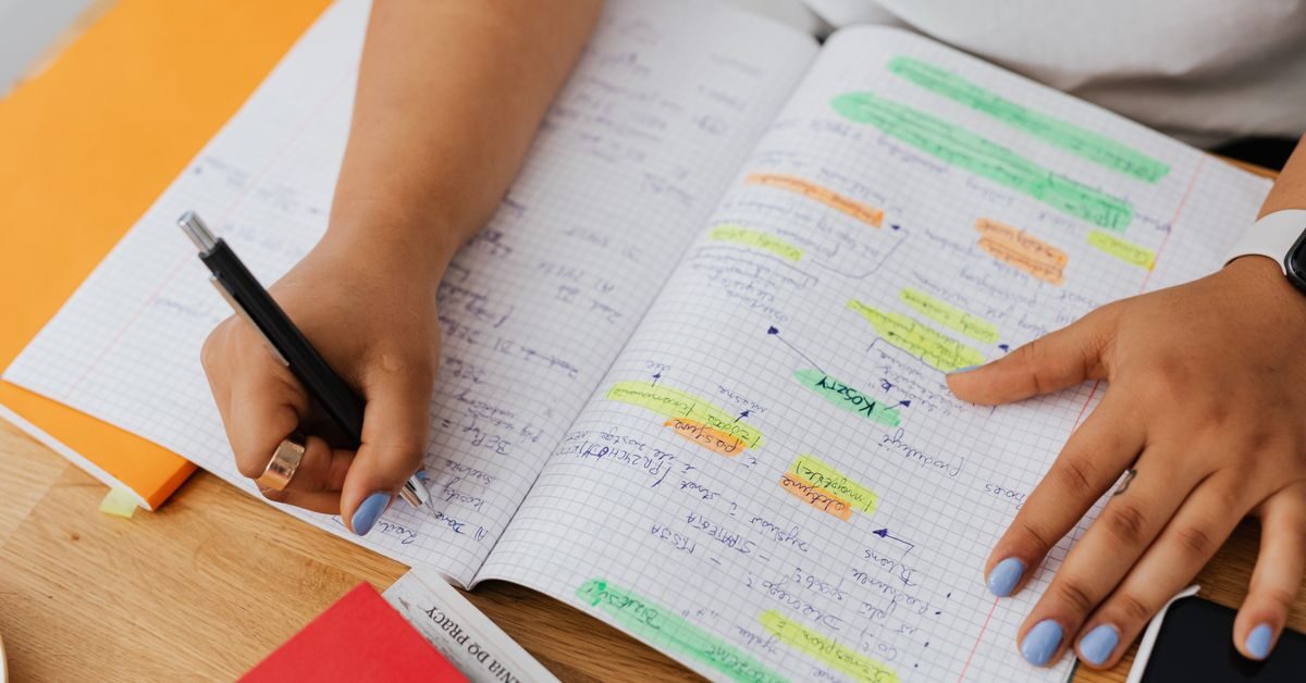 Student drafting how to write a thesis statement in a notebook at a desk