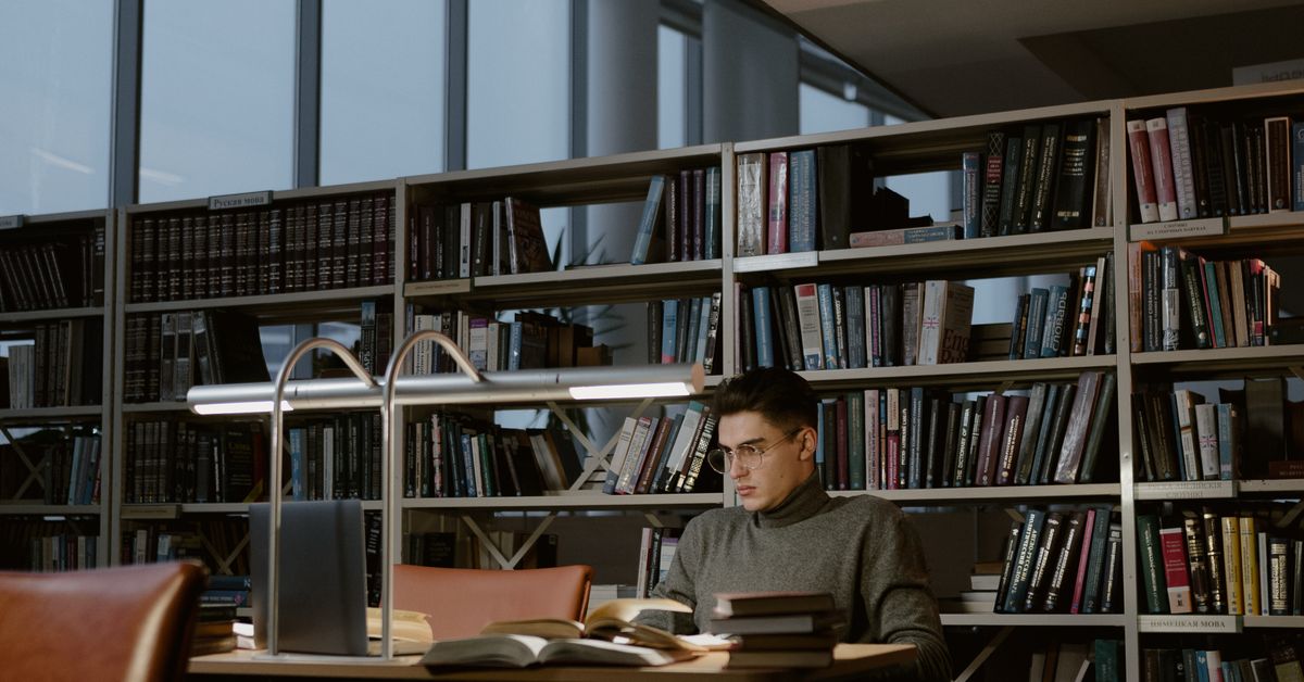 Student deeply engaged in study at a library desk surrounded by books