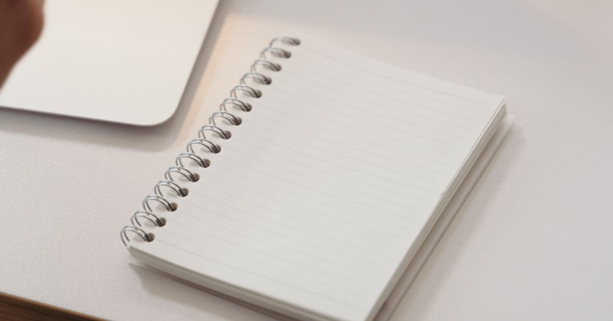 Research paper outline planned in a spiral notebook beside a laptop on a clean desk