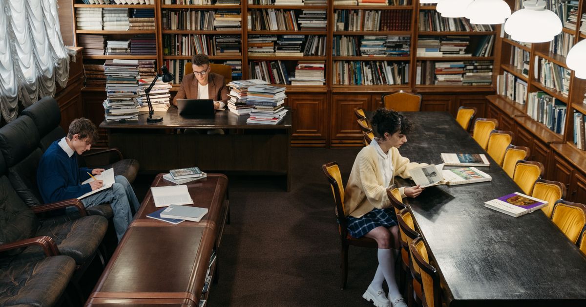 Three students studying together at a library table with books
