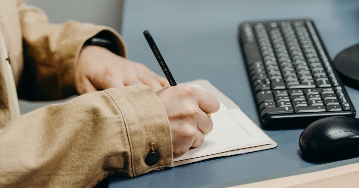 What is a thesis statement? Hands writing a draft thesis in a notebook on a desk